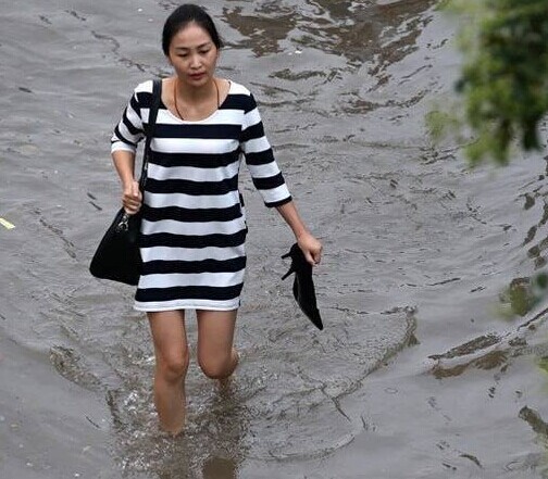一名女子脱下高跟鞋,涉水前行.