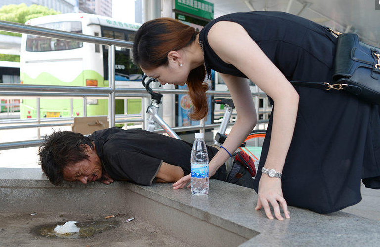 8月6日,在上海火车站南广场,一名流浪汉趴在花坛边呕吐,面露痛苦表情.