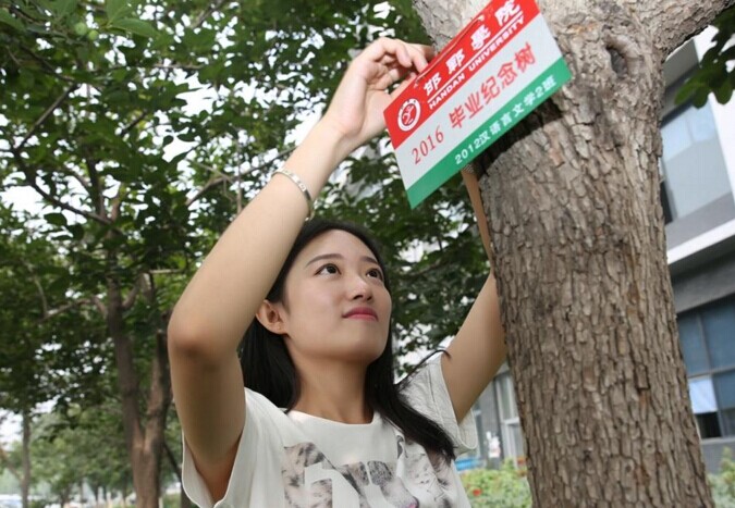 图为张钰桦在毕业季挂树牌活动上,把写有"2012汉语言文学2班"的纪念